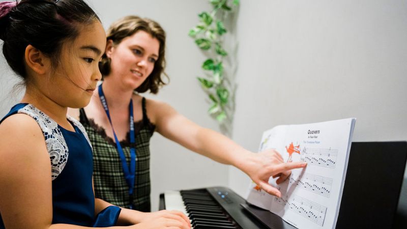 Giáo viên hướng dẫn học viên nhỏ tuổi luyện ngón trên đàn piano điện