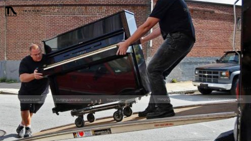 Nhân viên đang sử dụng đai hoặc xe chuyên dụng để di chuyển piano cơ