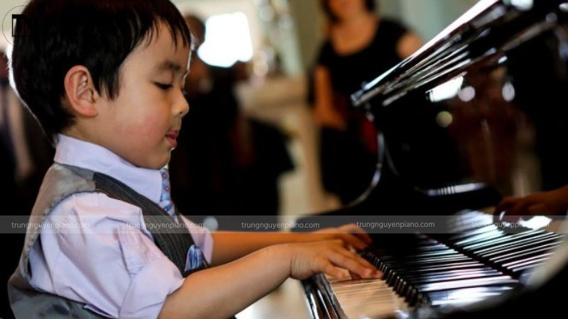 Một em bé đang ngồi bên phím đàn piano với ánh mắt mơ màng, sáng tạo