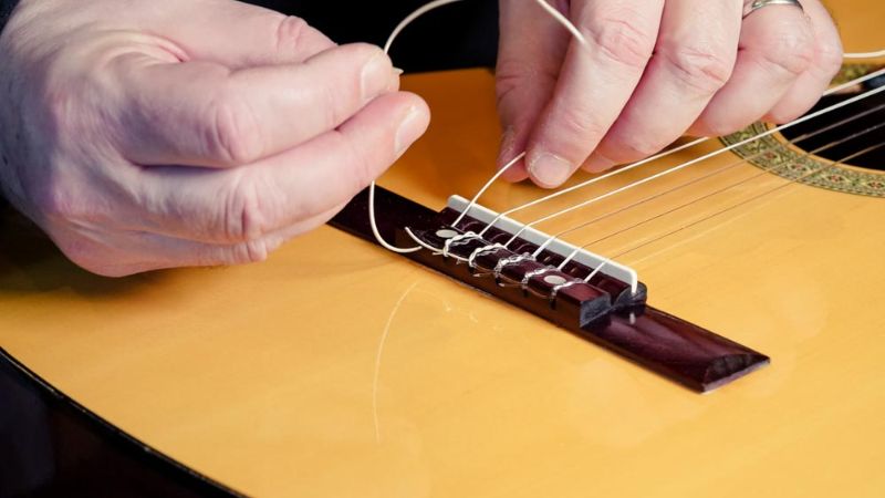 Kỹ thuật viên đang thay dây guitar, tháo dây cũ và lắp bộ dây mới đúng kỹ thuật